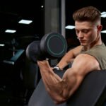 Fit young man doing One-Arm dumbbell preacher curl in the gym