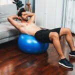 Athletic man doing abdominal crunches on a medicine ball in his Dubai Apartment
