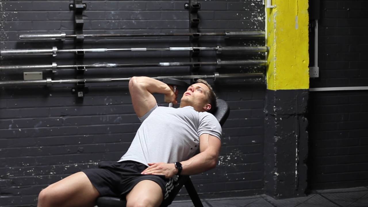 A young fit man doing a one arm dumbbell tricep extension