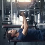 A young fit man in the gym doing Dumbbell Flys exercise on a bench