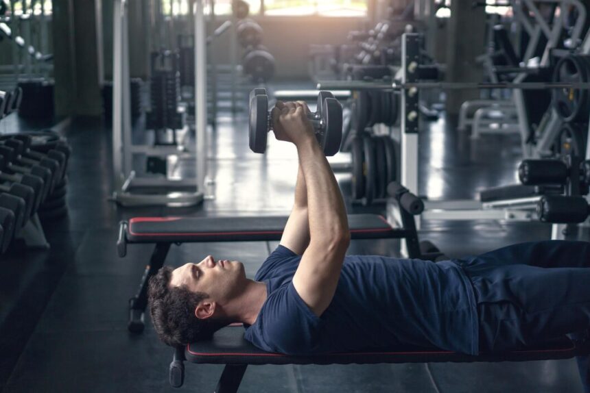 A young fit man in the gym doing Dumbbell Flys exercise on a bench