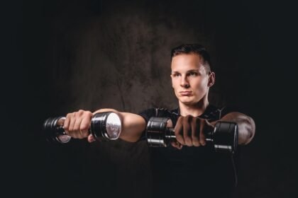 A young bodybuilder doing front raises with dark background