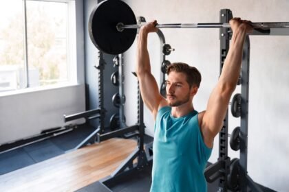 young man doing a military press in a gym: bodybuilding exercise
