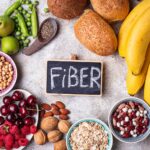 A colorful assortment of high-soluble fiber foods including oats, chia seeds, lentils, apples, bananas, and chickpeas, arranged on a rustic table.