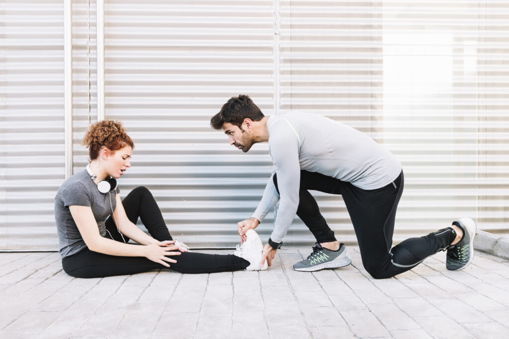 A personal trainer performing an assisted stretch on a female client's leg to correct muscle imbalances and improve knee mobility in order to achieve pain-free training.