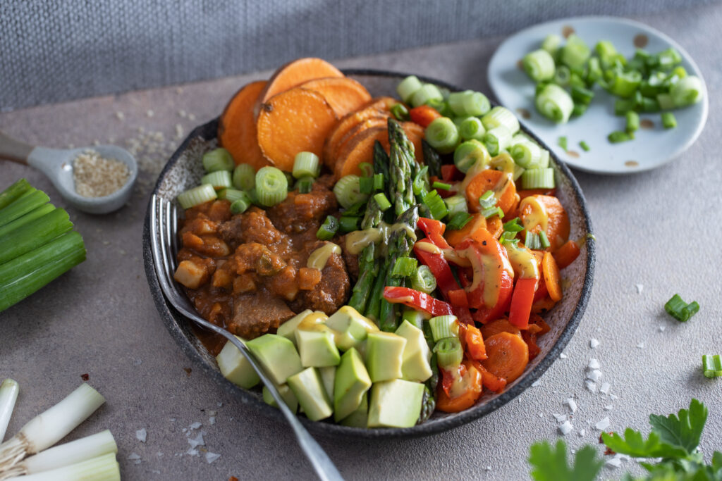 A delicious and balanced meal for hormone health featuring cooked beef cubes, roasted sweet potatoes, fresh asparagus, and sliced avocado on a plate.