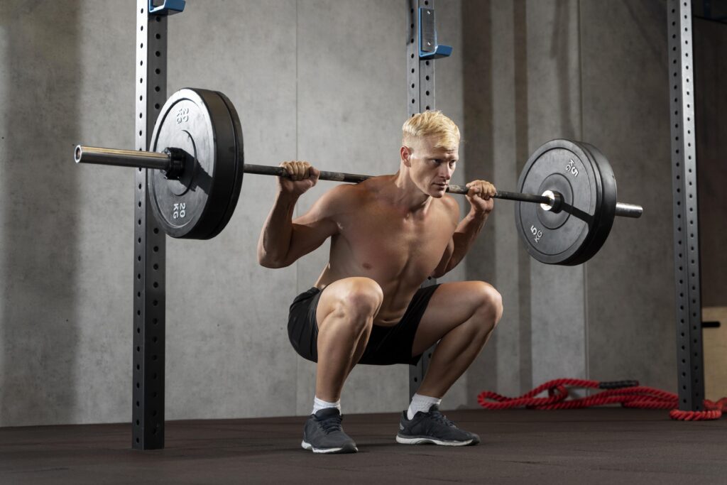 A determined male athlete performing a heavy barbell back squat in a gym, demonstrating proper form and intensity during a compound lift.