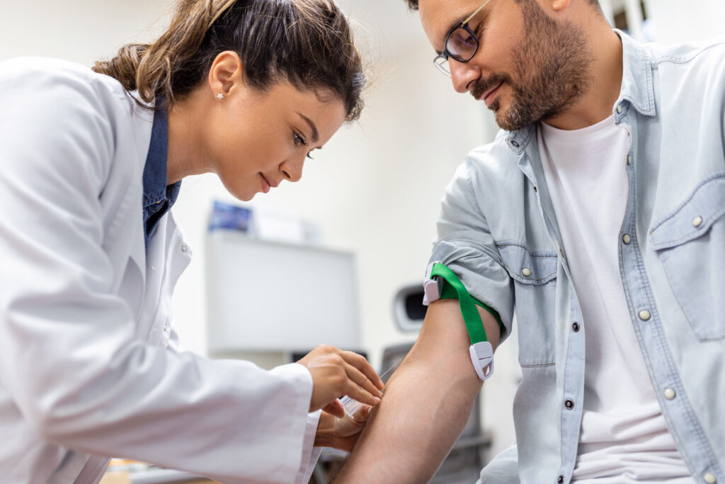 A female healthcare professional in a clinic gently drawing a blood sample from a male patient's arm for comprehensive hormone panel testing.
