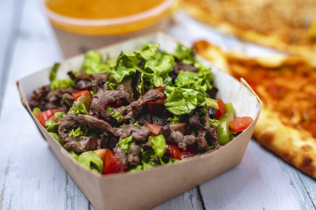 A healthy and colorful beef shawarma bowl in a Dubai restaurant, featuring grilled beef strips over a fresh salad, with sauce on the side.
