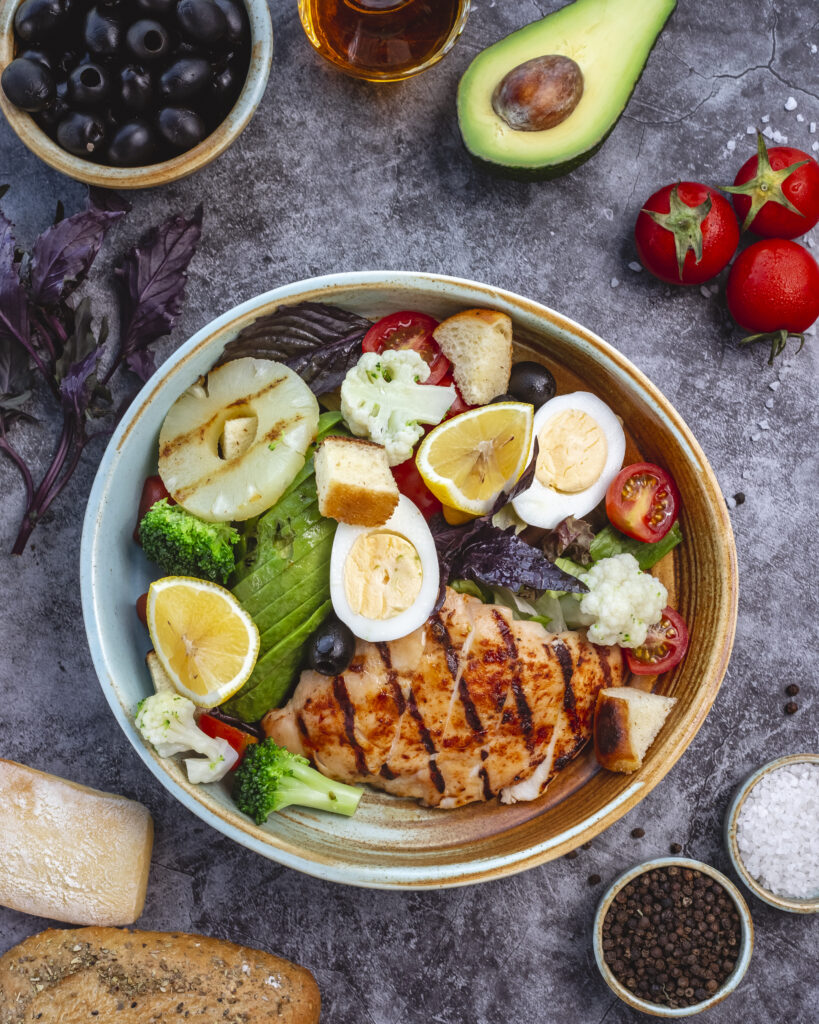 A clean, balanced meal for muscle growth featuring grilled chicken breast, fresh broccoli, sliced avocado, and boiled eggs on a white plate.