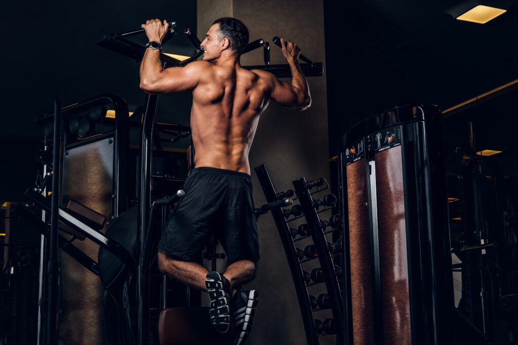 A muscular athlete performing a strict pull-up at the peak of contraction in a modern Dubai gym, showcasing full lat engagement for back width.